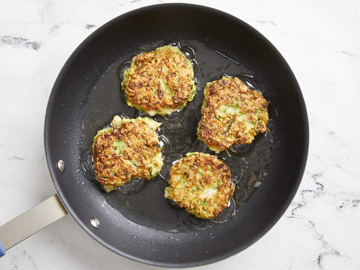 zucchini fritters flipped in pan.