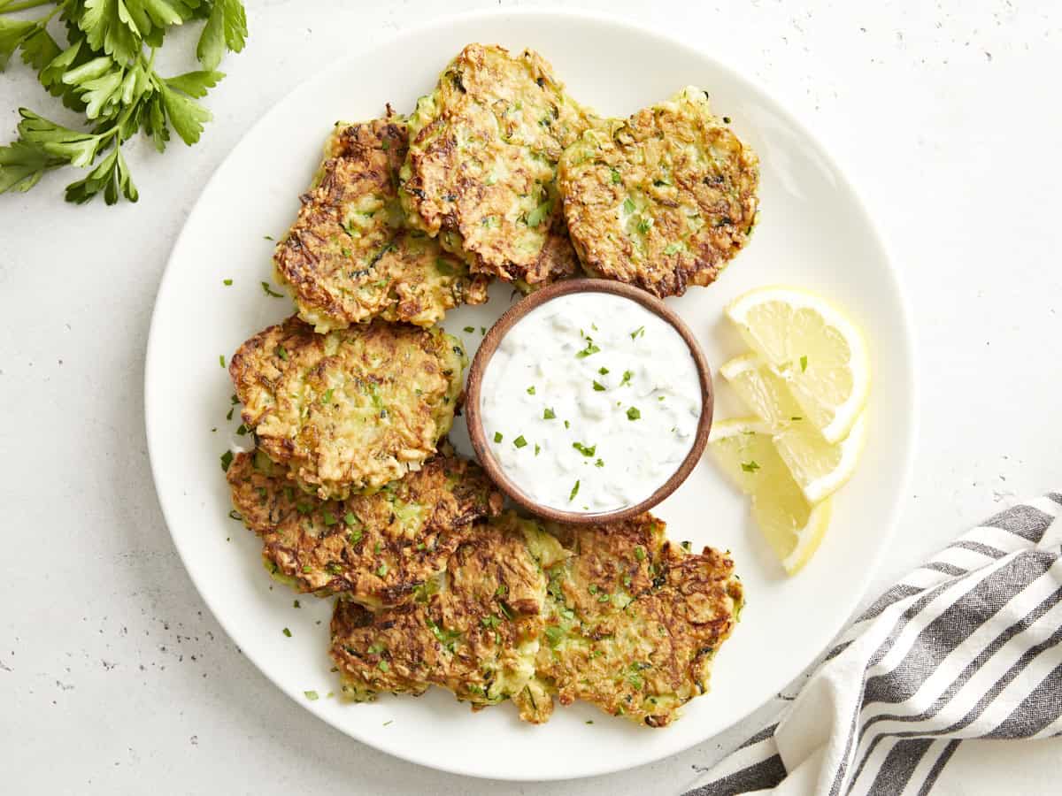 Overhead view of zucchini fritters on a platter served with tzatziki sauce.