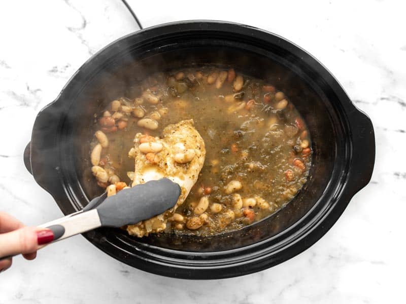 Chicken breast being removed from slow cooker with tongs