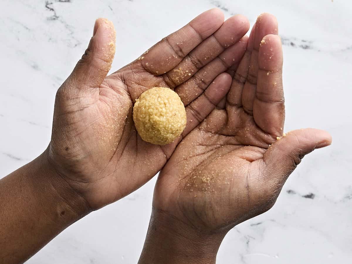 Hands handing a formed ball of matzo dough.