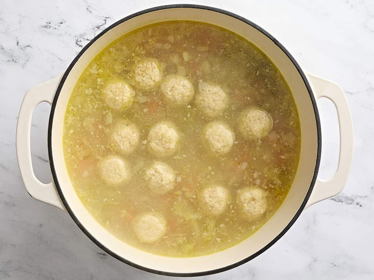 Matzo balls added to a sauce pot of chicken soup.