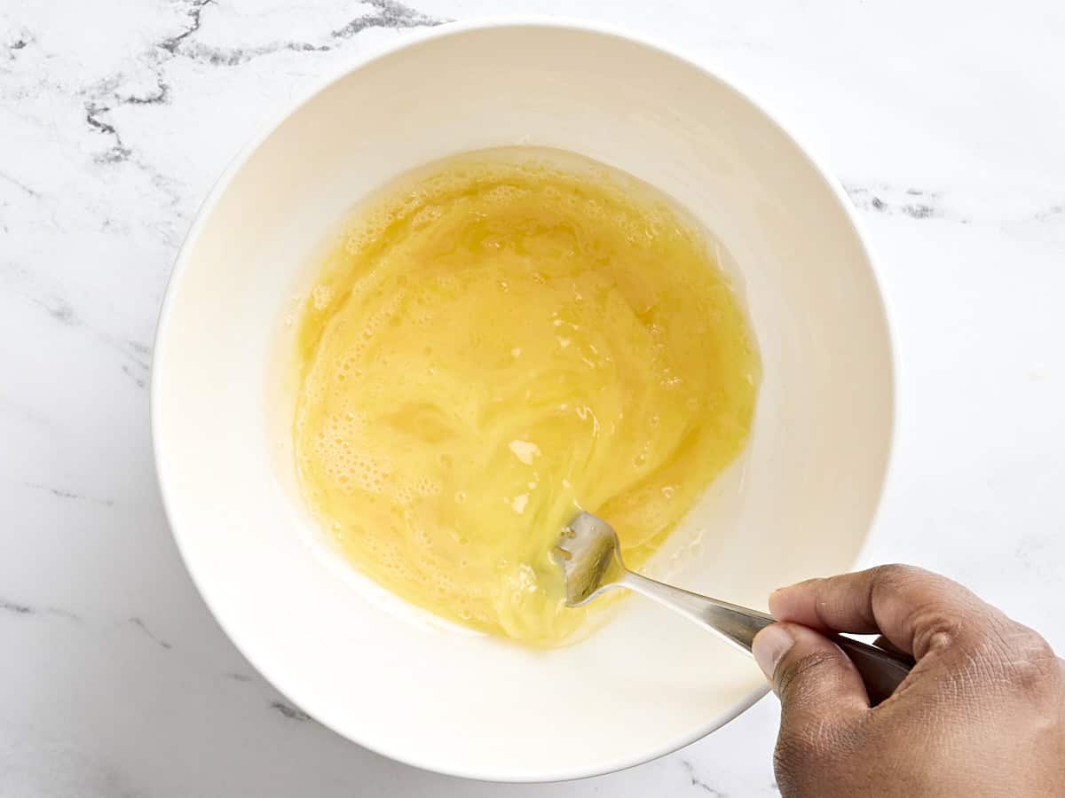 A fork mixing eggs and vegetable oil in a bowl.