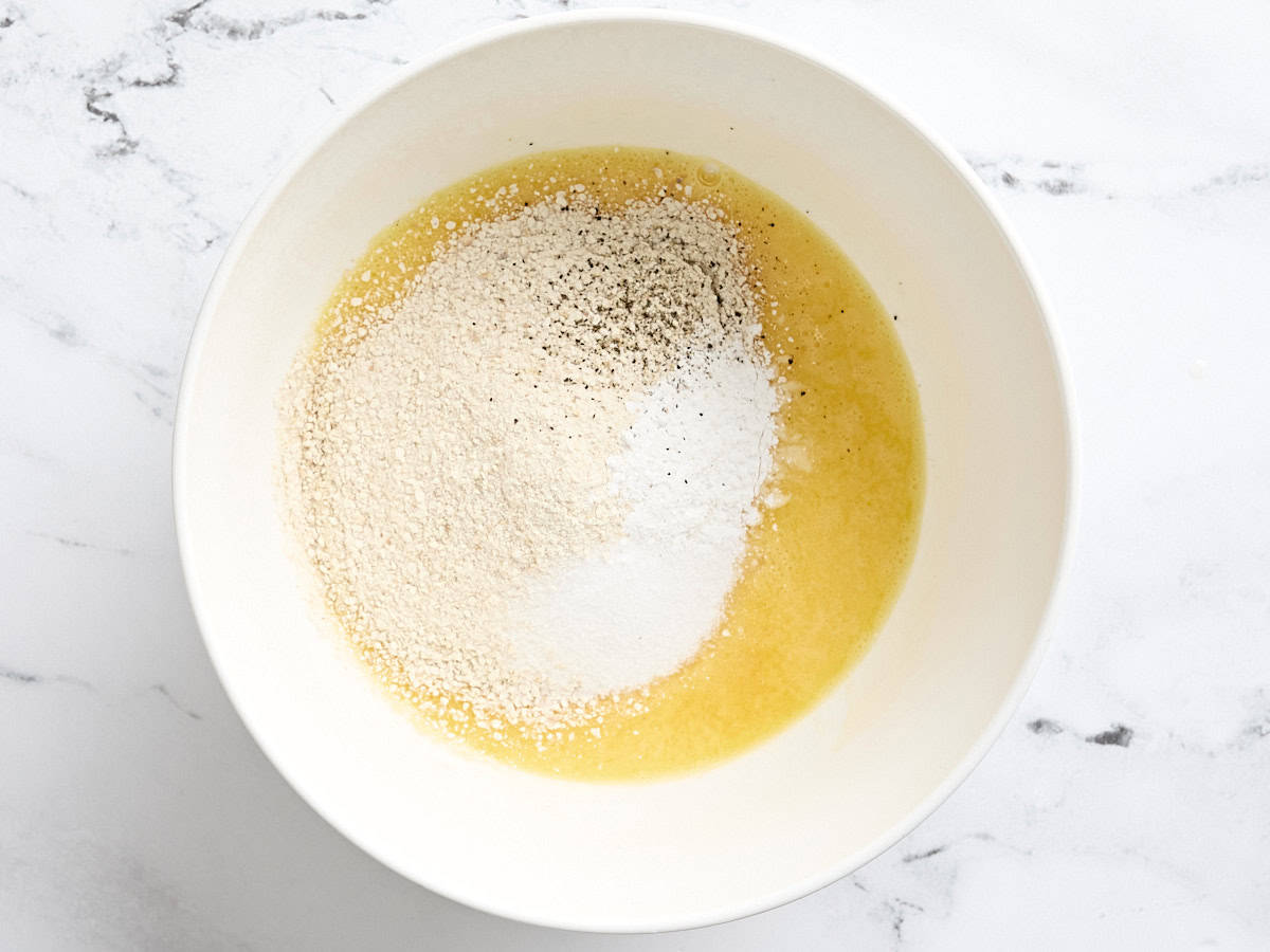 Matzo meal, salt, baking powder, and black pepper added to a bowl of whisked eggs.