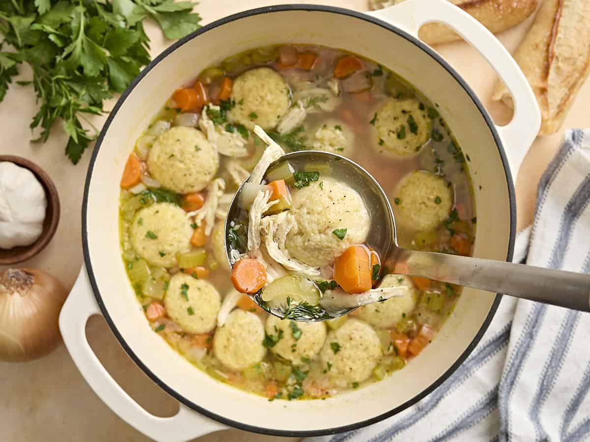 Overhead view of matzo ball soup in a sauce pot with a ladle.