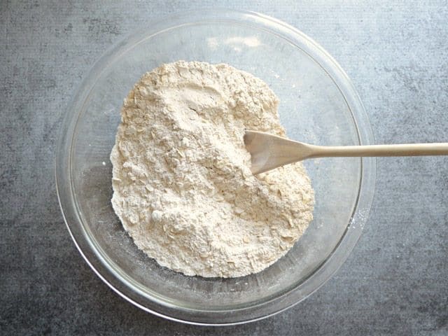 Dry ingredients for muffin batter in a glass bowl with wooden spoon