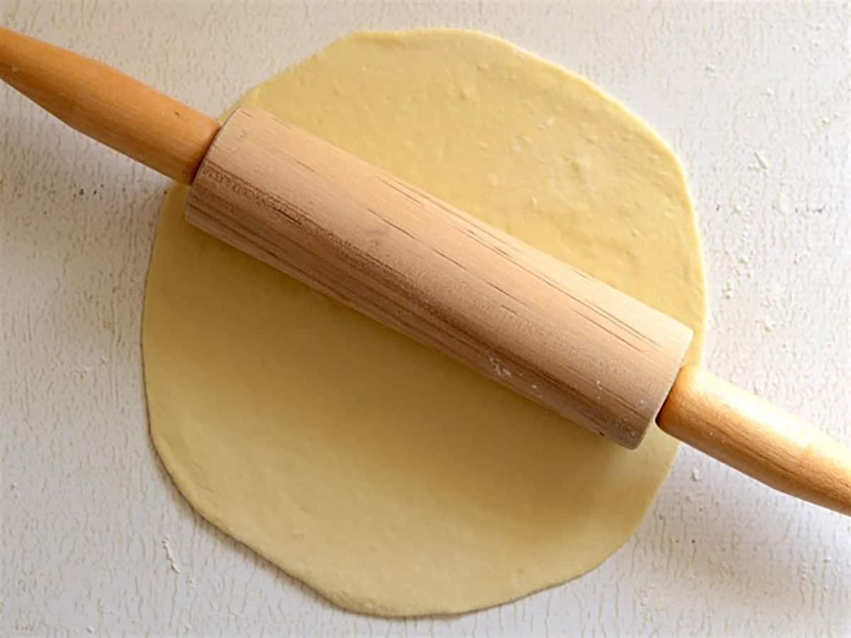 naan dough being rolled out with a rolling pin. 