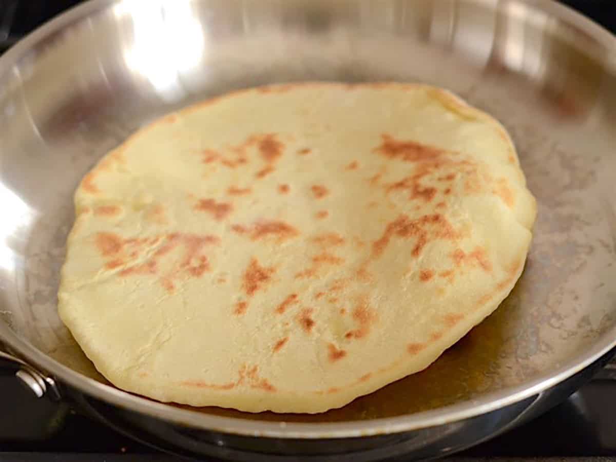 Naan flipped in the skillet to show the browned bottom. 
