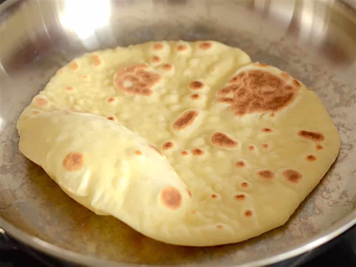 naan flipped in the skillet again to show the browned bubbles.
