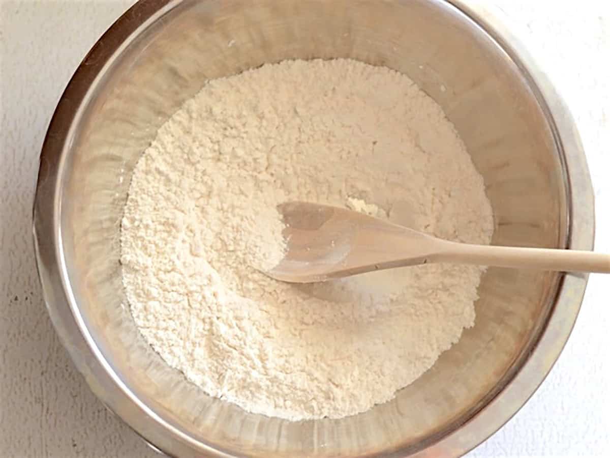 Flour and  salt mixed together in a metal bowl with a wooden spoon.