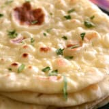 Close up side view of a stack of fresh naan garnished with parsley.