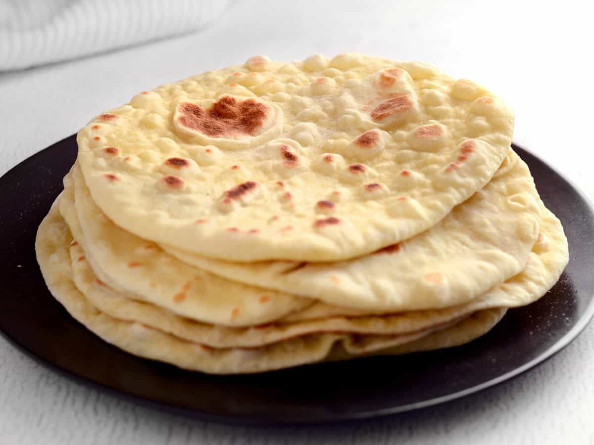 Cooked naan in a stack on a black plate. 
