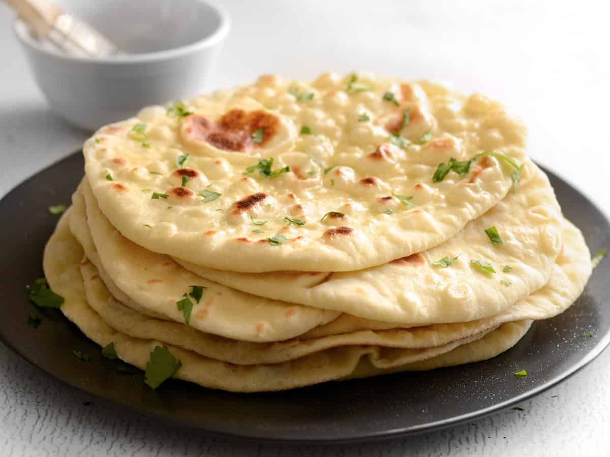 Side view of a stack of naan on a black plate, garnished with parsley.