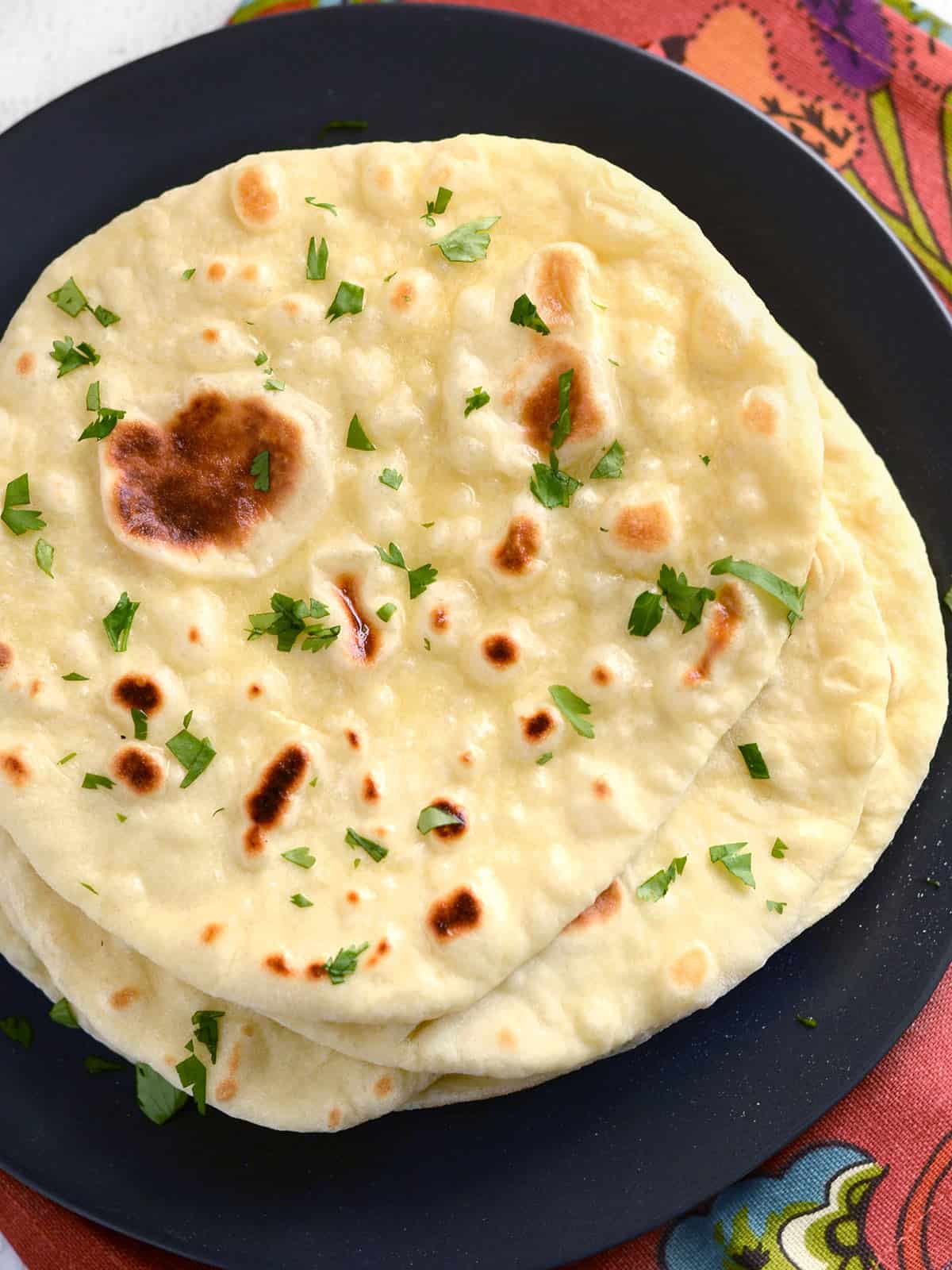Overhead view of a stack of naan on a plate garnished with parsley.