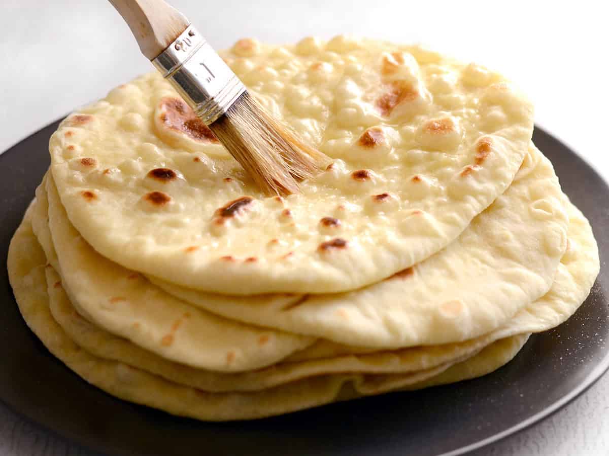 Stack of naan being brushed with melted butter.