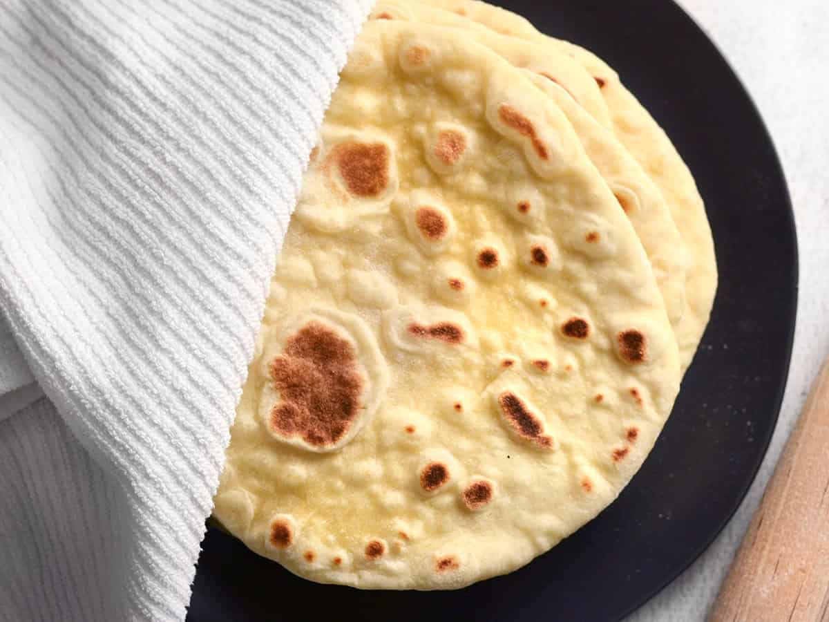 A stack of cooked naan on a plate covered with a towel to keep warm.
