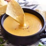 Nacho cheese sauce dripping off a chip into a bowl