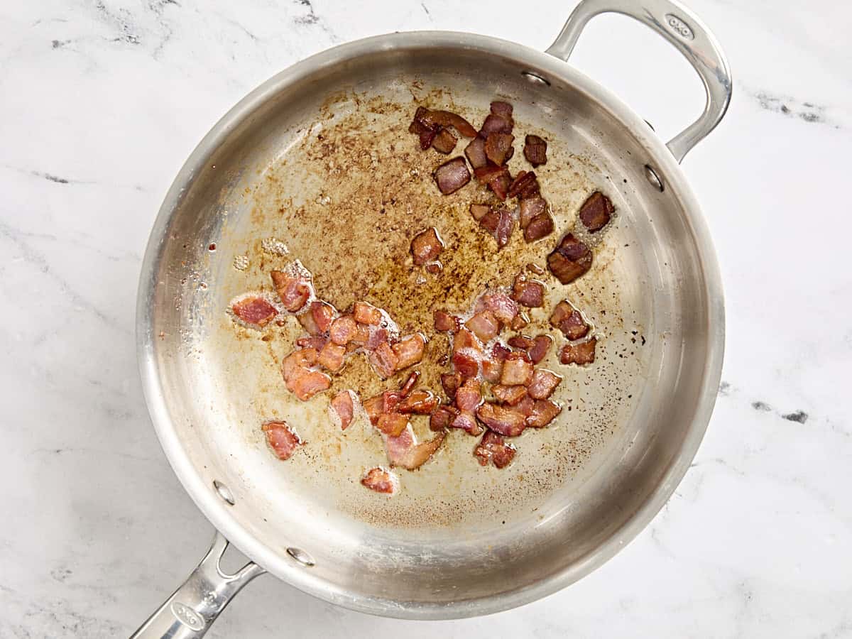 Diced bacon cooking in a skillet.