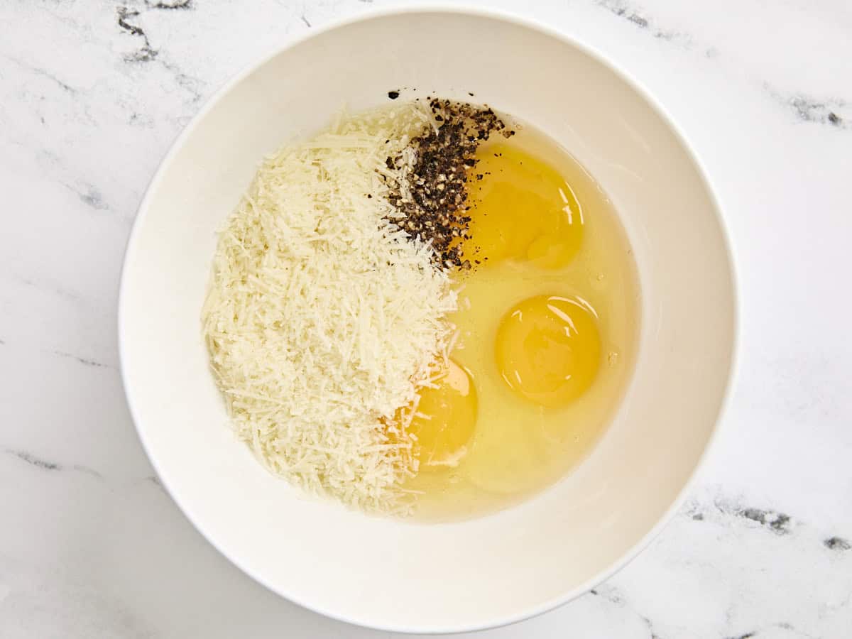 Shredded parmesan, black pepper, and eggs in a mixing bowl.