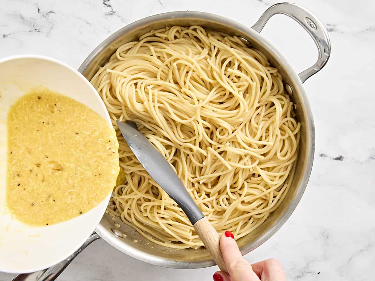 Egg and cheese mixture being poured into cooked spaghetti in a skillet.