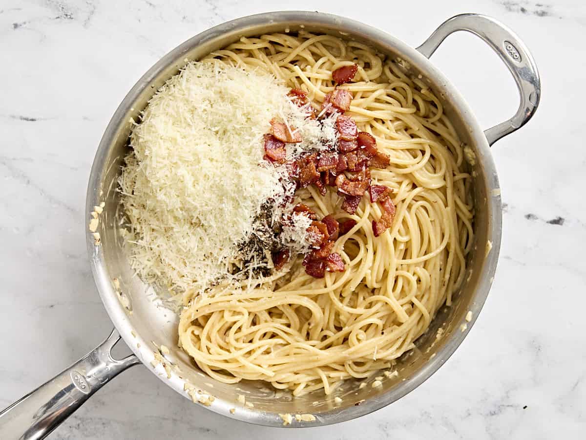 Shredded parmesan, cooked bacon, and fresh parsley added to cooked spaghetti in a skillet.