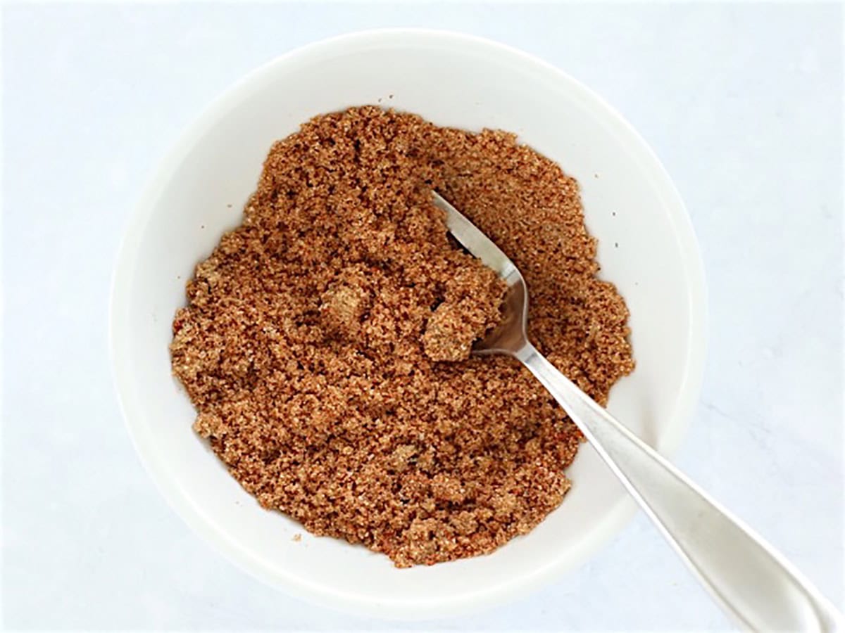 Close up view of brown sugar and spices mixed in a white bowl with a fork.