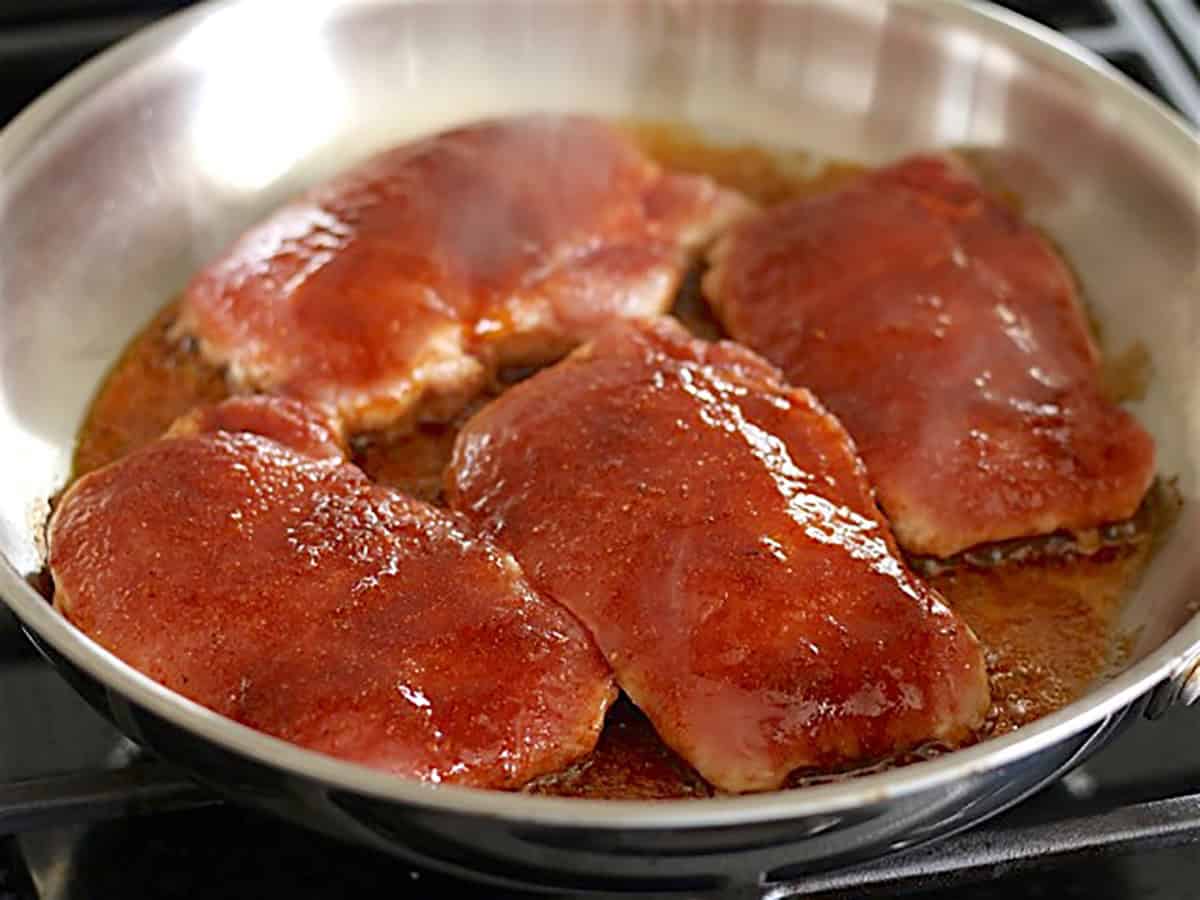 Seasoned boneless pork chops in a skillet, half cooked.