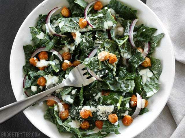 Overhead view of a Kale Salad with Cajun Spiced Chickpeas and Buttermilk Dressing in a white bowl on a black surface.