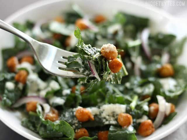 Close up of a forkful of Kale Salad with Cajun Spiced Chickpeas and Buttermilk Dressing with the bowl in the background.
