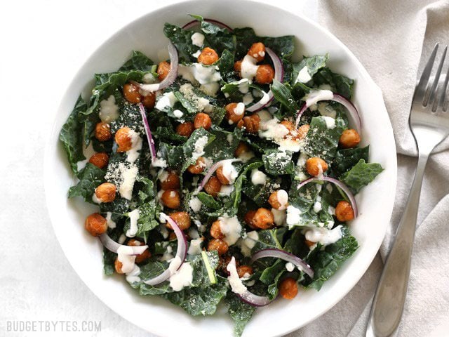 Overhead view of a white bowl of Kale Salad with Cajun Spiced Chickpeas and Buttermilk Dressing on a white background