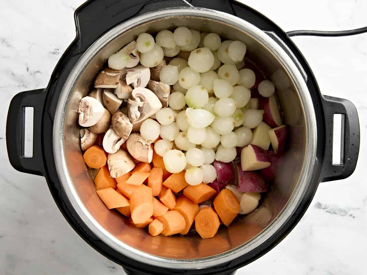 Pearl onions, diced carrots, and mushrooms added to an Instant Pot.