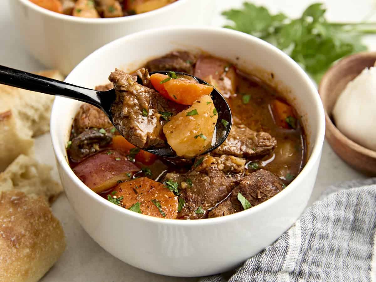 Side view of a bowl of beef stew with some on a spoon.