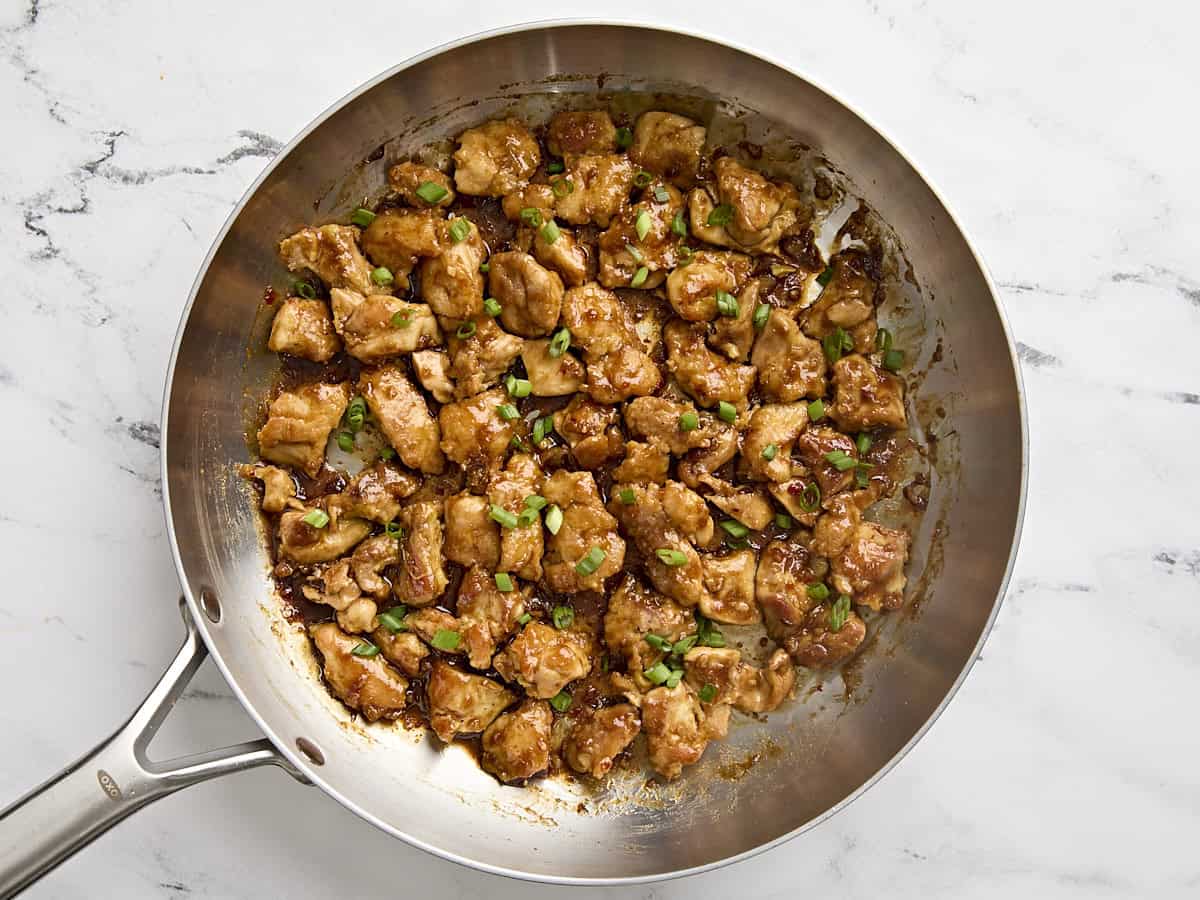 Finished orange chicken in a skillet, garnished with sliced green onions.