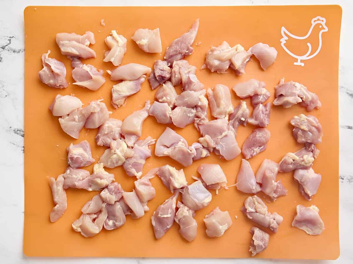 Diced chicken thighs on a cutting mat.