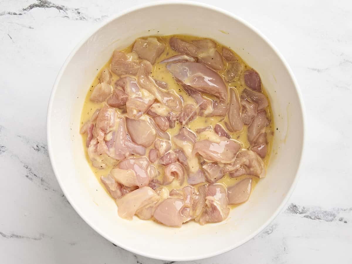 Diced chicken thigh pieces in a cornstarch and egg mixture in a mixing bowl.