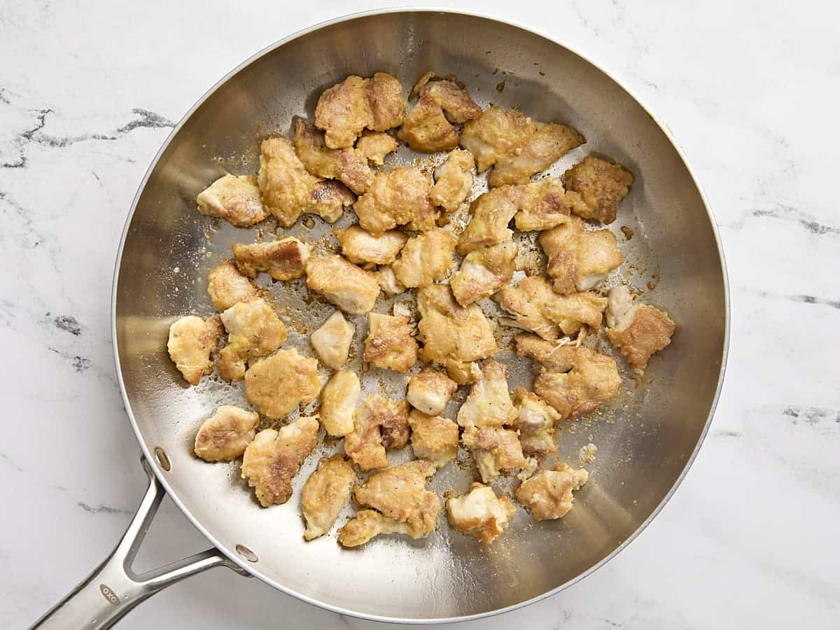 Chicken thigh pieces cooking in a skillet.