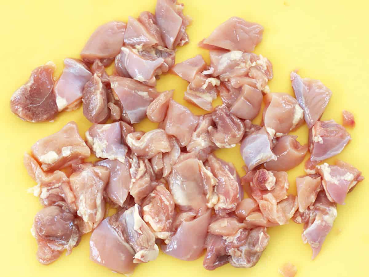 Diced chicken thighs on a yellow cutting board. 