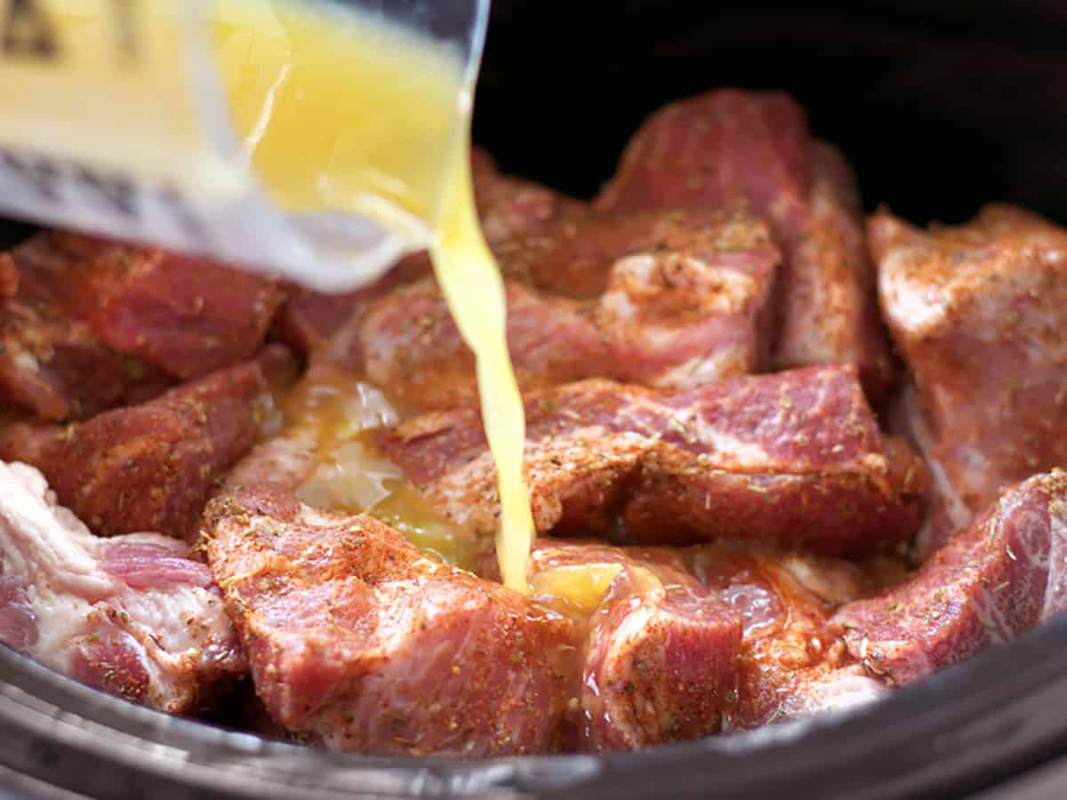 orange juice being poured into the slow cooker on top of the pork.