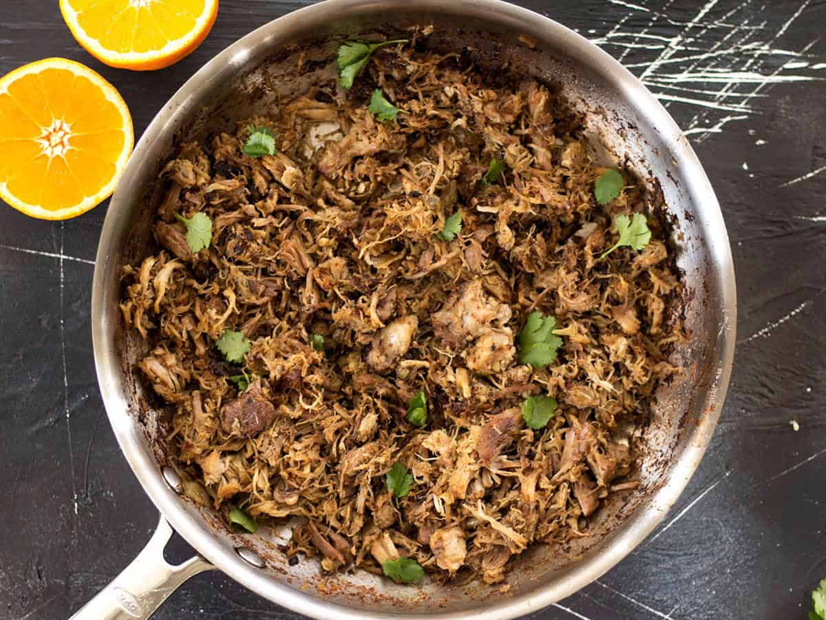 Overhead view of a skillet full of slow cooker carnitas with an orange on the side.