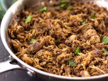 Close up of carnitas in a skillet garnished with cilantro.