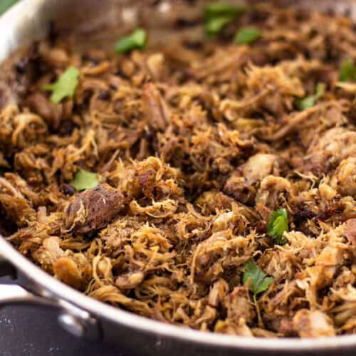 Close up of carnitas in a skillet garnished with cilantro.