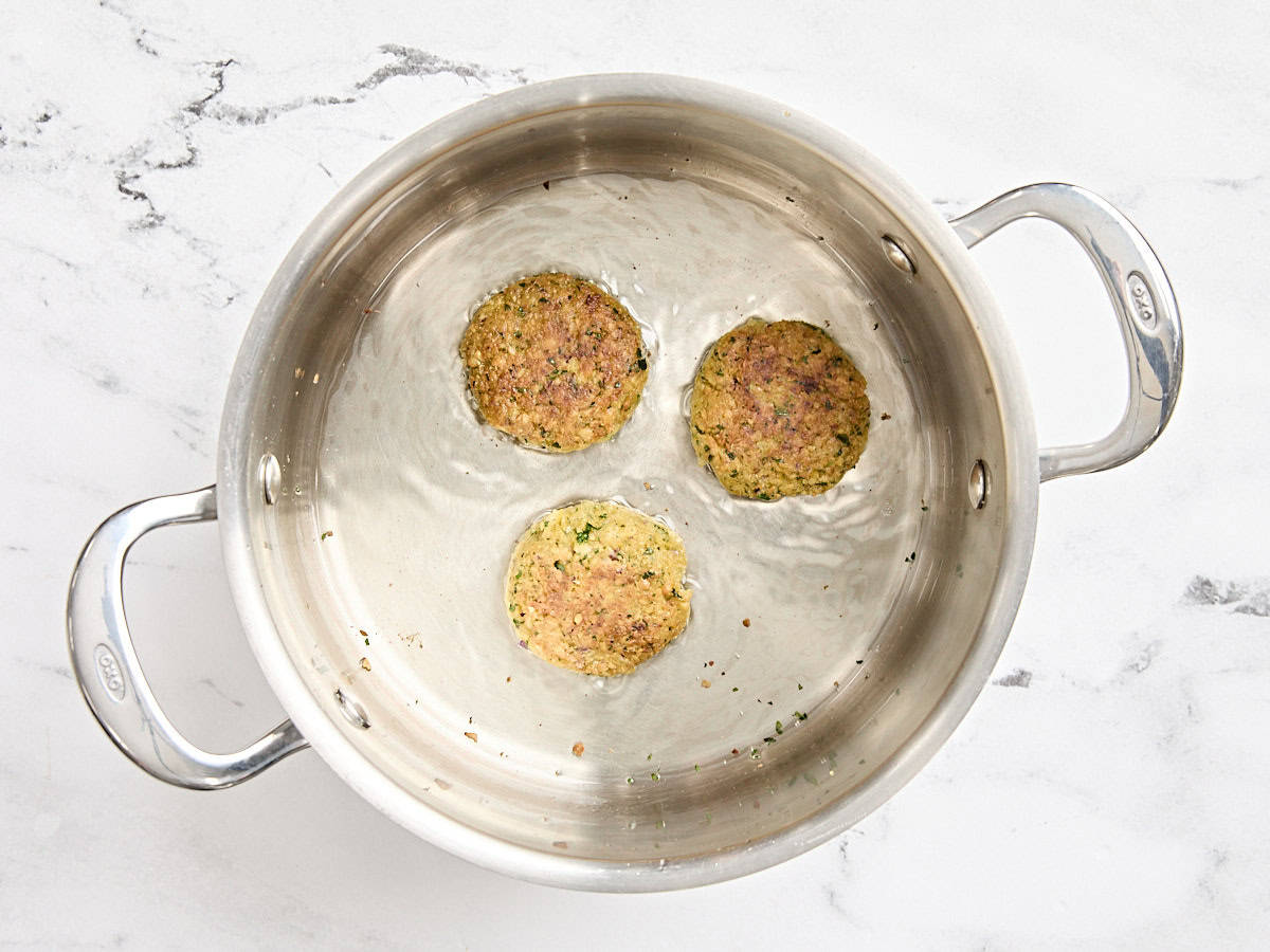 Three falafel patties frying in a pan of oil.