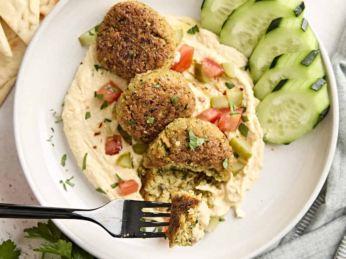 A fork taking some homemade falafel from a bed of hummus with salad.