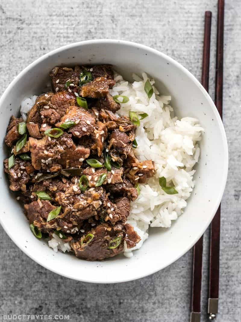 A bowl of Slow Cooker Sesame Beef served with rice and garnished with green onion and sesame seeds