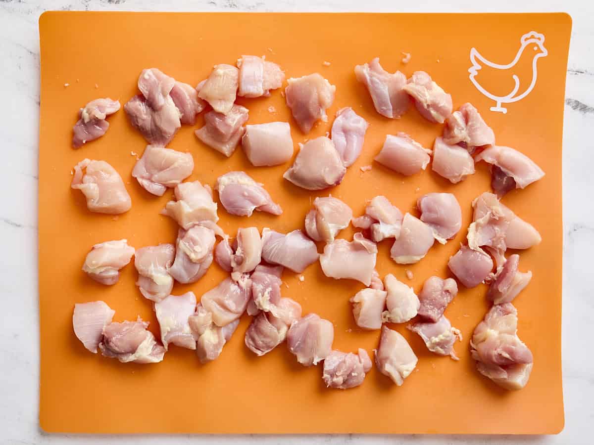 Diced raw chicken thighs on a meat preparation mat.