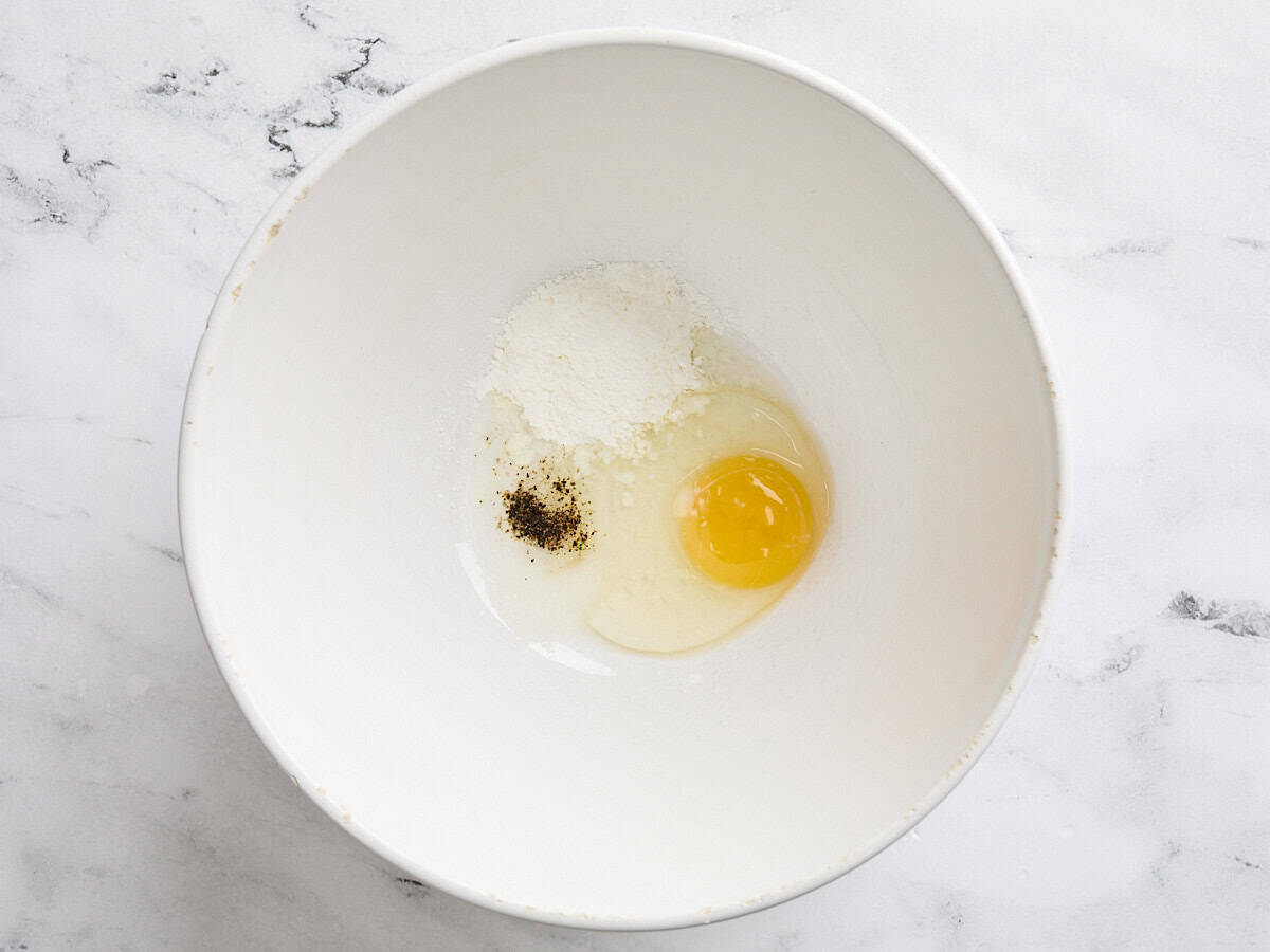 A cracked egg, corn starch, and seasonings in a mixing bowl.