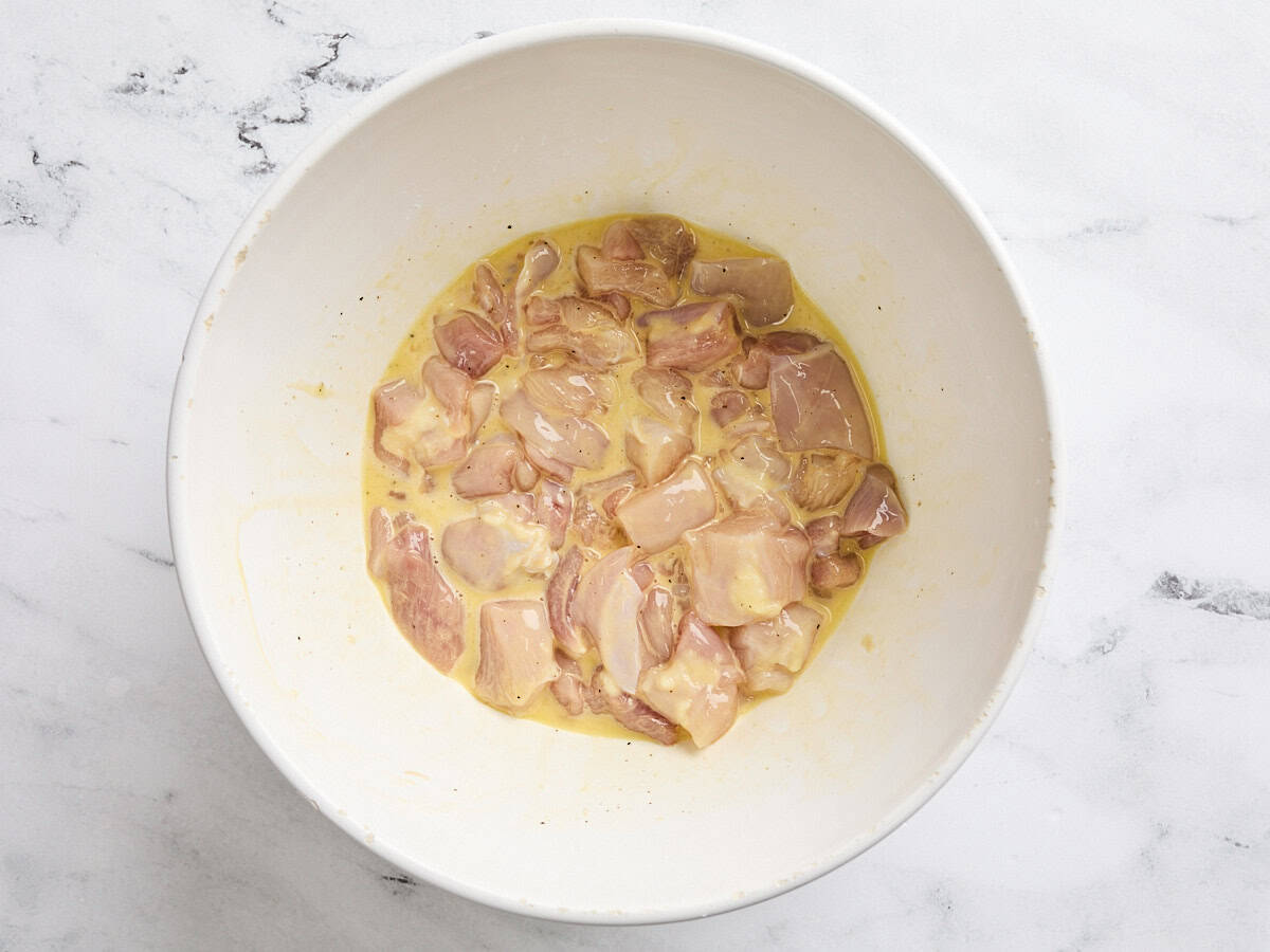 Raw diced chicken breast in a bowl with the cornstarch and egg mixture.