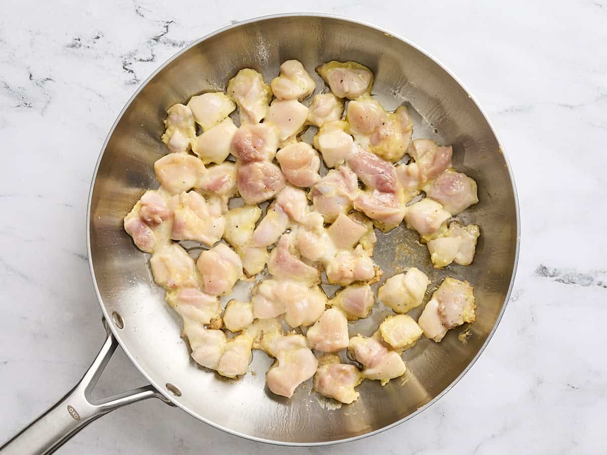 Coated chicken thigh pieces cooking in a skillet.