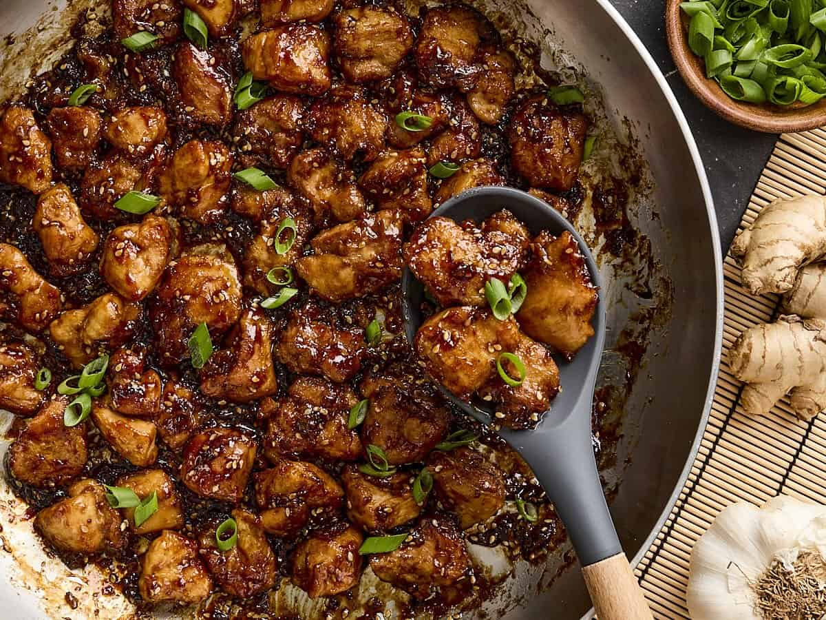 Overhead close up of homemade sesame chicken in a skillet with a serving spoon.