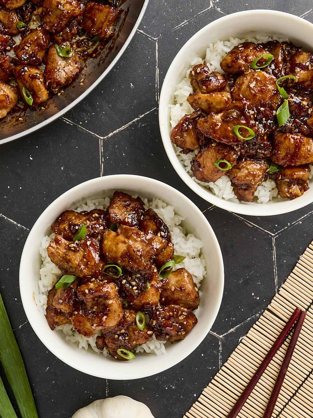 Overhead view of sesame chicken in bowls with rice.