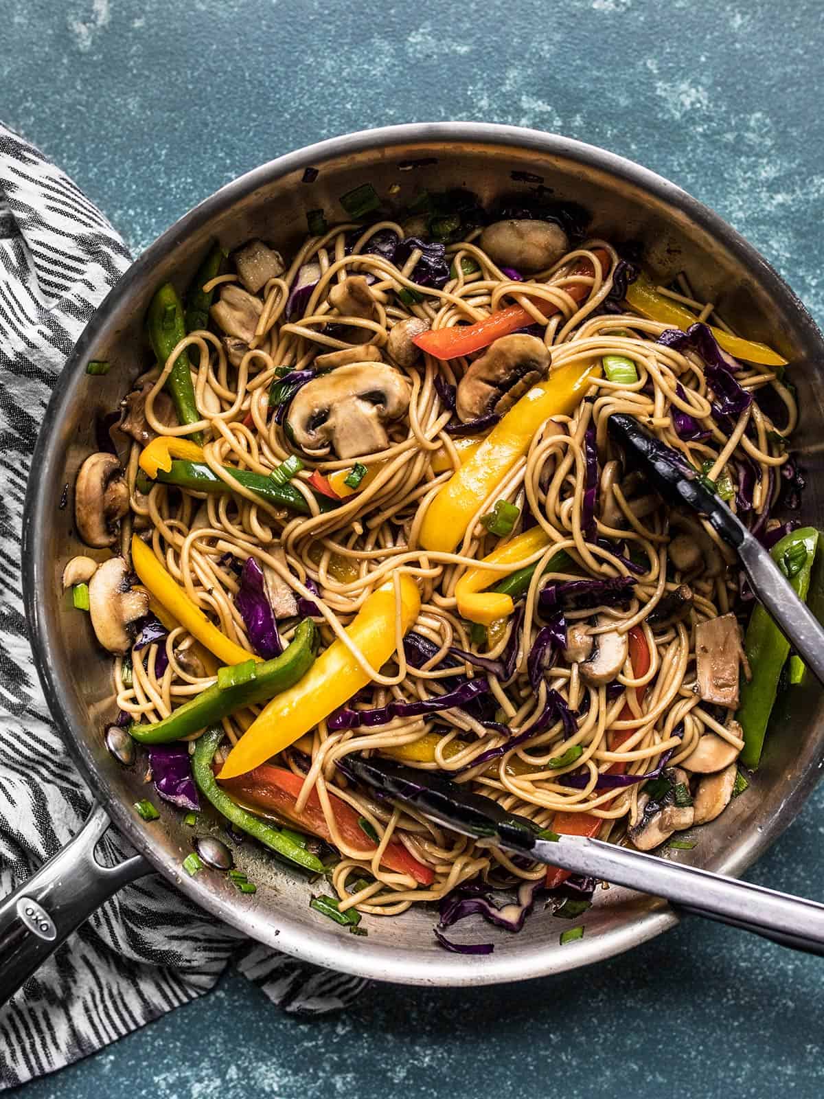 Overhead view of a skillet full of vegetable lo mein with tongs.